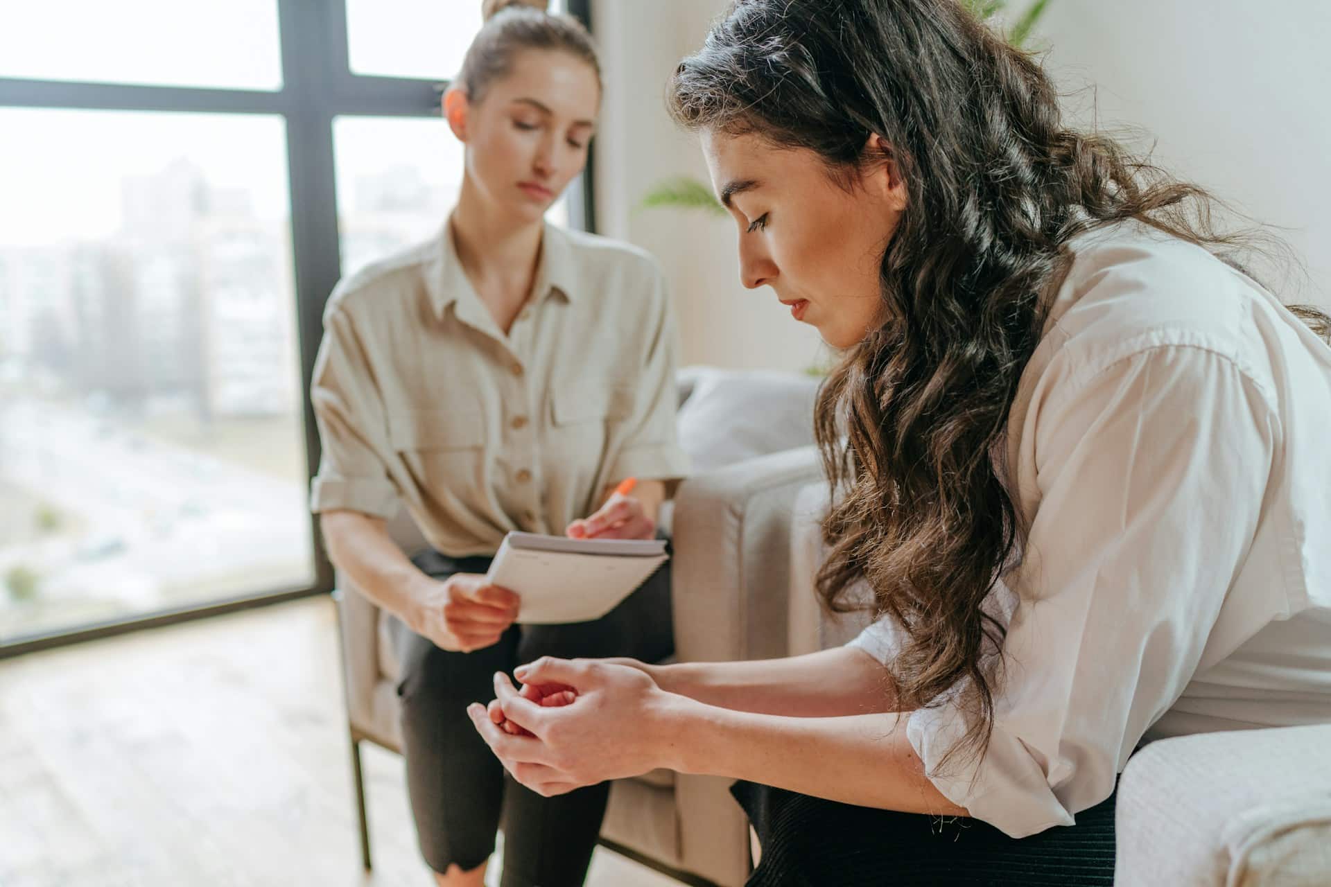 Twee vrouwen zitten in een kamer met een groot raam. De een, met een klembord, kijkt aandachtig, terwijl de ander nadenkend met gevouwen handen zit. De setting suggereert een counselingsessie gericht op de organisatie, gericht op het stimuleren van vitaliteit door middel van een doordacht gesprek. Twee vrouwen zitten in een kamer met een groot raam. De een, met een klembord, kijkt aandachtig, terwijl de ander nadenkend met gevouwen handen zit. De setting suggereert een counselingsessie gericht op de organisatie, gericht op het stimuleren van vitaliteit door middel van een doordacht gesprek.