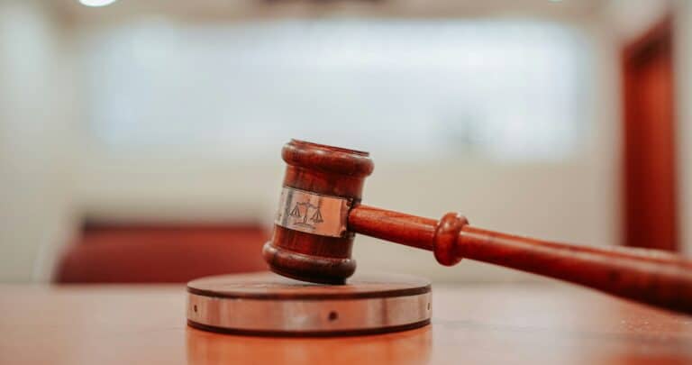 A wooden judge’s gavel rests on a sound block atop a table in a courtroom, with blurred lights and benches in the background—capturing the solemn atmosphere where law firms like Wijn & Stael pursue justice.