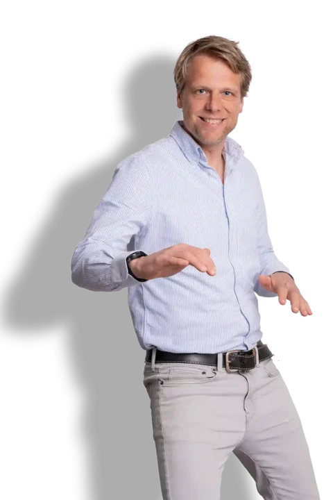 Een lachende man met blond haar, Harro Yestra, draagt een lichtblauw gestreept shirt en een lichtgrijze broek. Hij poseert speels met gebogen armen tegen een witte achtergrond.