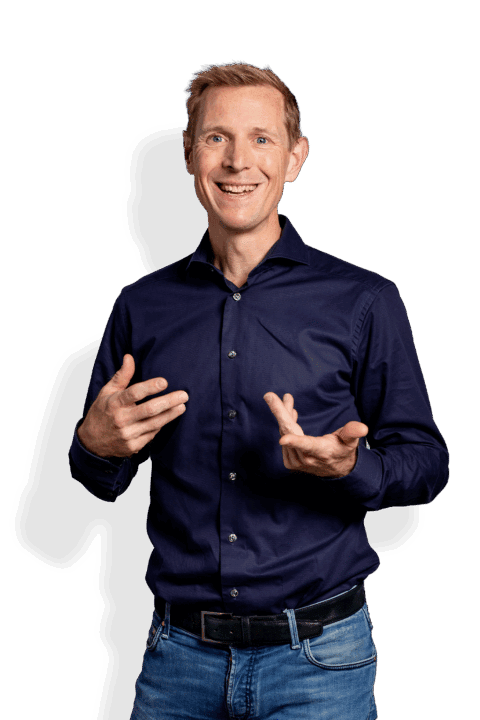 Een lachende man met kort blond haar, die een donkerblauw overhemd met knoopsluiting en een spijkerbroek draagt, gebaart met beide handen terwijl hij naar voren kijkt - hij lijkt op Jochem Uytdehaage.