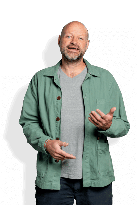 Een kale man met een baard, die een lichtgrijs T-shirt en een groen jack draagt, staat met zijn gezicht naar de camera en maakt glimlachende gebaren met één hand - dit is Tjarko Erdtsieck.