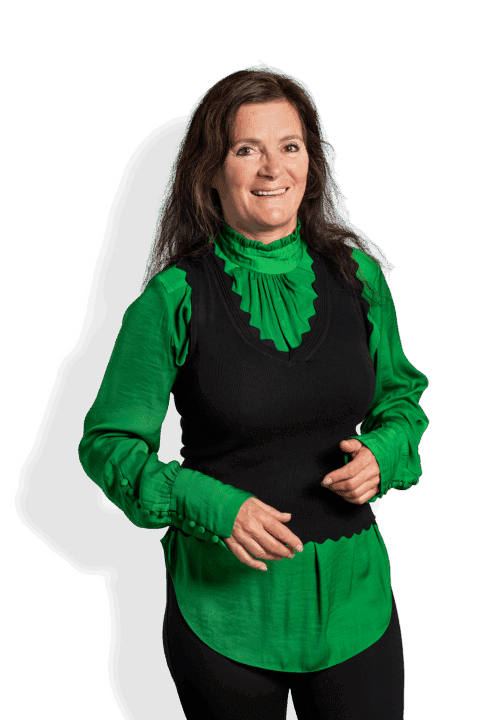 Een vrouw met lang bruin haar, in een felgroene blouse met ruches onder een zwart mouwloos vest, staat glimlachend met haar handen omhoog bij haar middel - klaar om de rechtszaak Koosje tegen Frankenhuysen te bespreken.