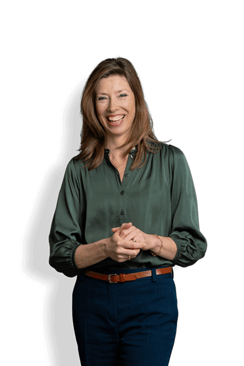 Ellen Egging, eine Frau mit hellbraunem Haar, die eine grüne Bluse und dunkelblaue Hosen trägt, steht lächelnd mit vor der Brust gefalteten Händen da.