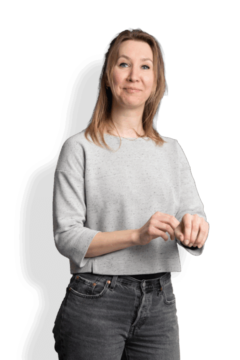 Simone van Beekveld, eine Frau mit hellbraunem Haar, trägt einen hellgrauen Pullover und schwarze Jeans. Sie steht vor einem weißen Hintergrund, lächelt leicht und hält ihre Hände vor sich zusammen.