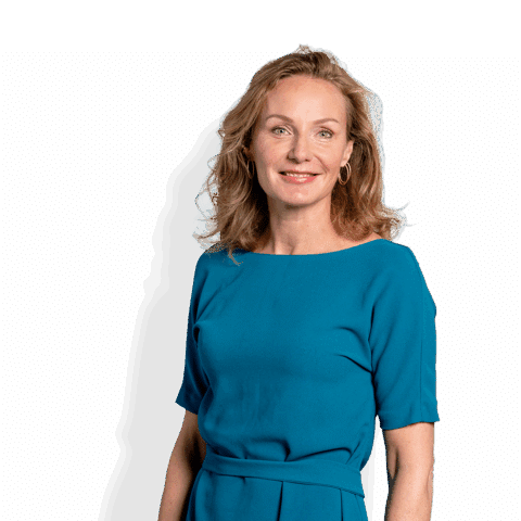 Een vrouw met golvend blond haar in een groenblauwe jurk staat tegen een effen witte achtergrond en glimlacht zachtjes naar de camera - de warmte van een topmoeder in elk programma.